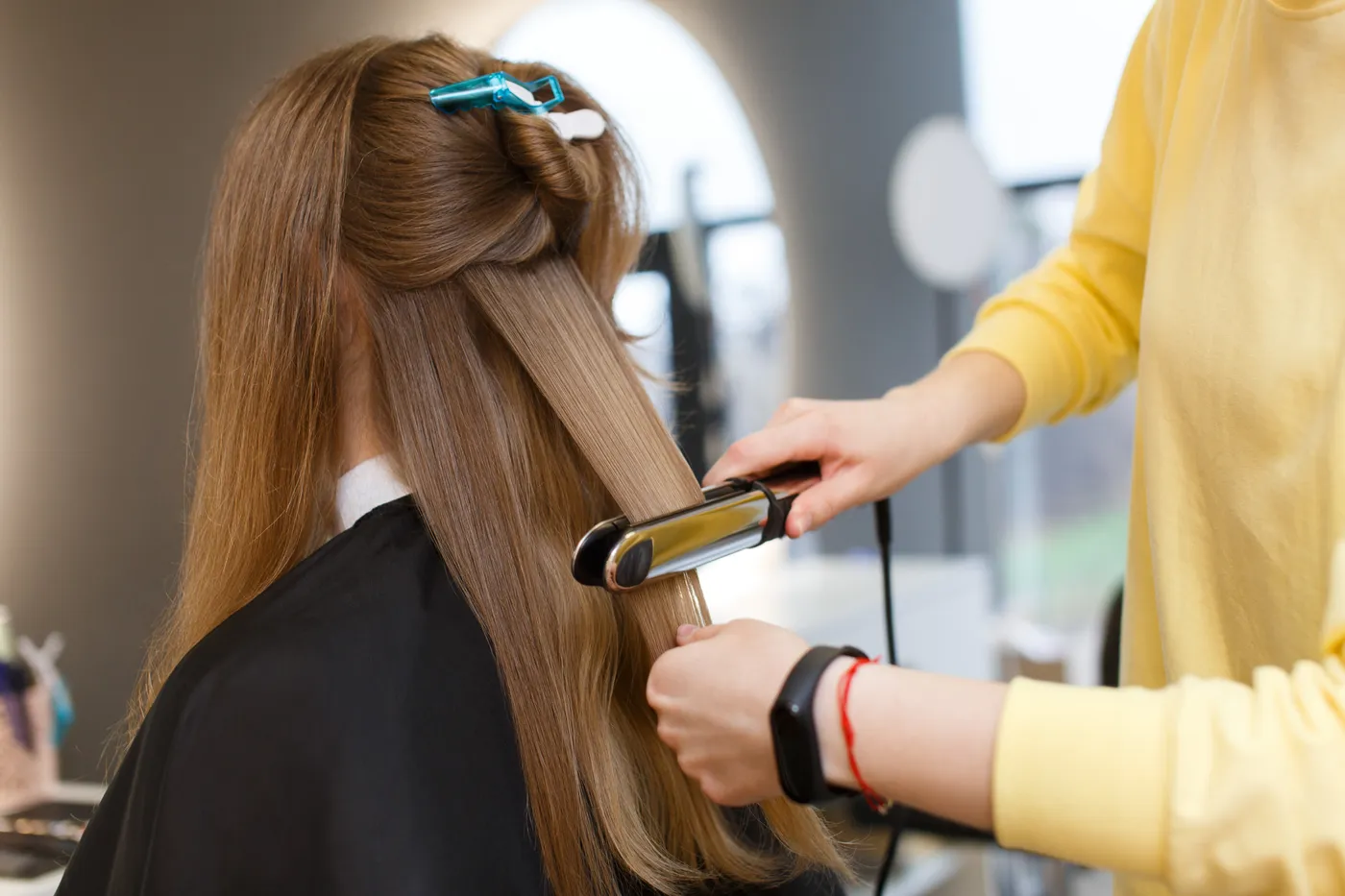 Frizerka z ravnalnikom zapira keratin v strukturo lasu v frizerskem salonu